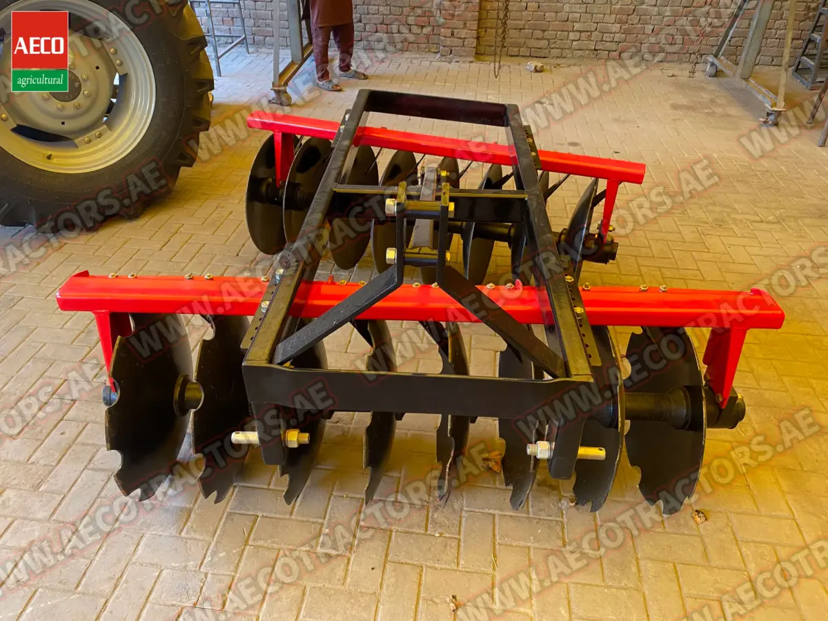 Three-point hitch system on an Aeco disc harrow connected to a Massey Ferguson tractor in a farm setting.